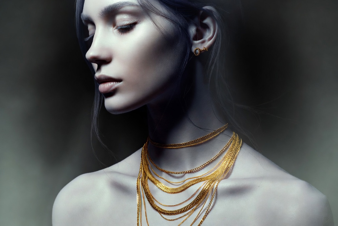 woman with glowing skin wearing layered gold necklaces and simple gold earrings