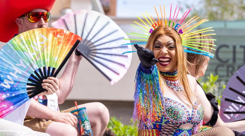 Group of drag queens in elaborate costumes and makeup, joyfully posing at a Pride celebration